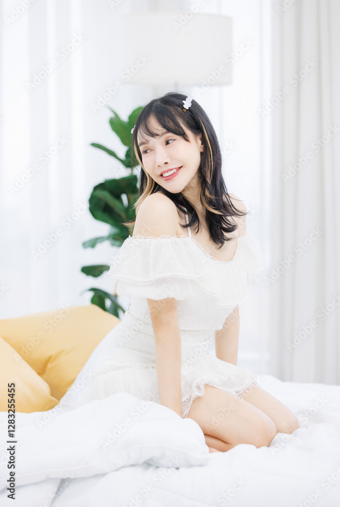 Asian happy young beautiful cheerful female sitting on cozy white bed smiling looking around in bedroom at home, Good morning calm comfortable healthcare relaxing resting well being peaceful concept. Asian happy young beautiful cheerful female sitting on cozy white bed smiling looking around in bedroom at home, Good morning calm comfortable healthcare relaxing resting well being peaceful concept.