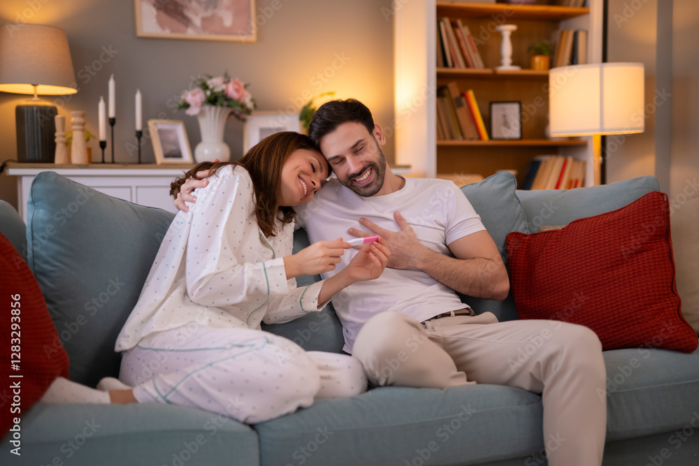 Cheerful couple looking at positive pregnancy test, sitting on bed Cheerful couple looking at positive pregnancy test, sitting on bed