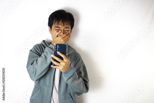 Asian teenager in white t-shirt and blue hoodie, posing sadly looking at the contents of his cellphone