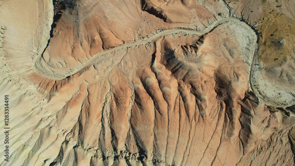 Aerial view of a winding desert road cutting through colorful rock formations in the rugged landscape of utah, showcasing the beauty of nature's artistry