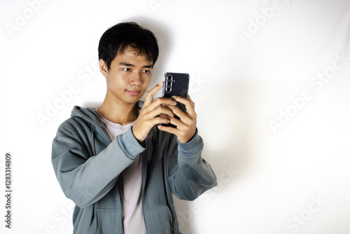 Asian teenager in white t-shirt and blue hoodie, posing taking pictures with his cellphone