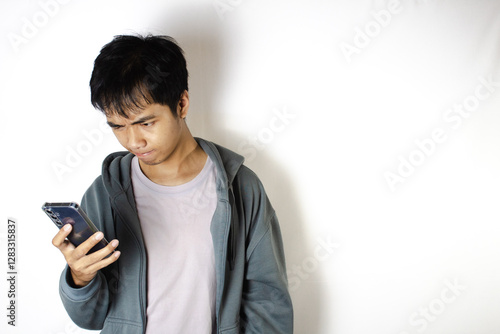 Asian teenager in white t-shirt and blue hoodie, posing focused on looking down at his cellphone