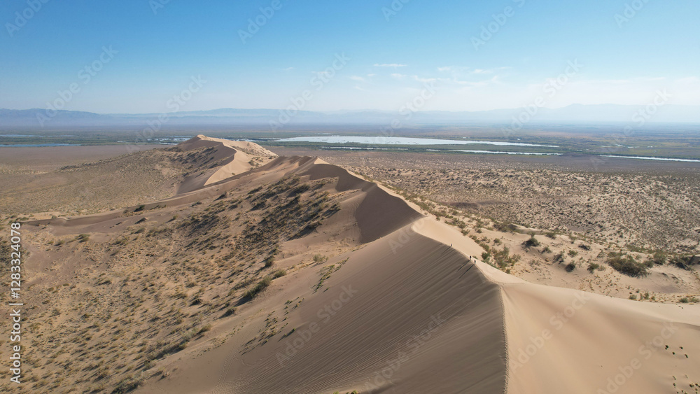 Tourists are hiking along the crest of the singing barkhan, a giant sand dune in altyn-emel national park, known for emitting a low-pitched humming sound in dry weather