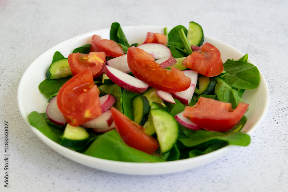 Raw fresh green healthy organic salad of spinach, cucumber, tomato and radish in white bowl on table top view on grey background. Raw fresh green healthy organic salad of spinach, cucumber, tomato and radish in white bowl on table top view on grey background.