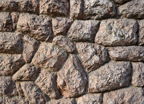 Detailed view of a stone wall showcasing natural texture and color variations in sunlight