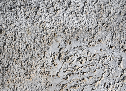 Texture of weathered concrete wall showcasing unique patterns and natural erosion marks in bright sunlight