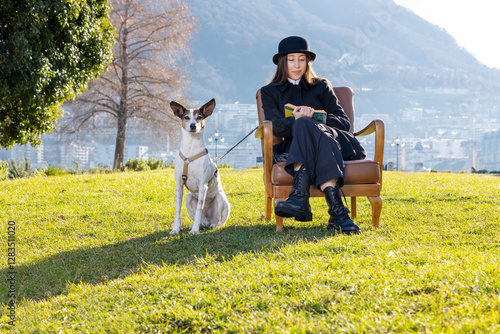 Quadro em tela Portrait of a beautiful girl sitting in an armchair in a public park with a very obedient dog next to her