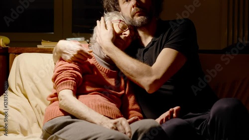 Elderly care. Caregiver son assisting elderly mother with cognitive decline. Neurodegenerative disease and mental health concept. Adult son caressing and hugging old mother