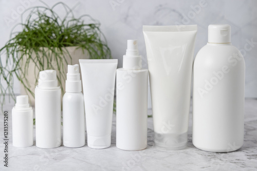 White cream bottles and tubes on white marble table near green plant close up, cosmetic mockup photo