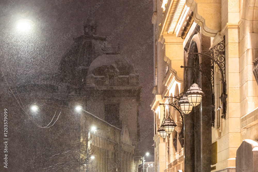 Winter in Bucharest. A snow-covered street in Bucharest illuminated by vintage street lamps, casting warm light on the cold winter night.