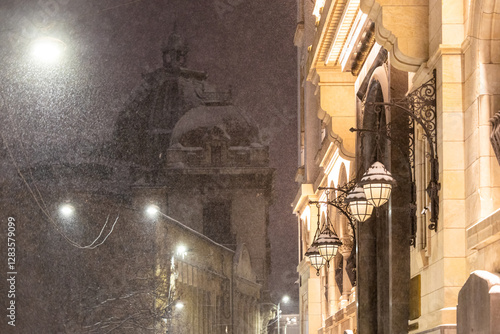 Obraz na płótnie Winter in Bucharest. A snow-covered street in Bucharest illuminated by vintage street lamps, casting warm light on the cold winter night. w salonie