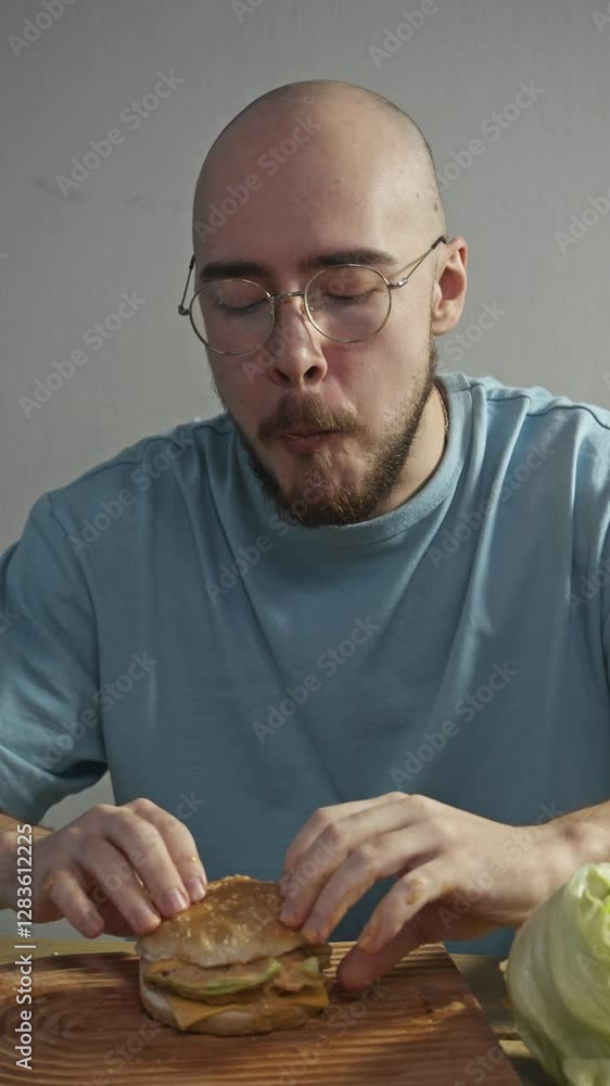 Bald man casually stuffs large portion of hamburger into his mouth, trying to overeat. He then happily licks his fingers, which are now covered in sauce, savoring unhealthy dish. he gives thumbs up Bald man casually stuffs large portion of hamburger into his mouth, trying to overeat. He then happily licks his fingers, which are now covered in sauce, savoring unhealthy dish. he gives thumbs up