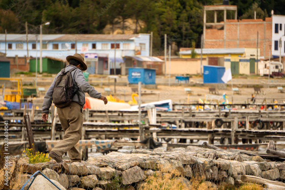 Local Bolivian Man Walking on the Stone Pier of Copacabana Bolivia with a Picturesque View of the Wooden Docks Lining the Harbor of Lake Titicaca Local Bolivian Man Walking on the Stone Pier of Copacabana Bolivia with a Picturesque View of the Wooden Docks Lining the Harbor of Lake Titicaca