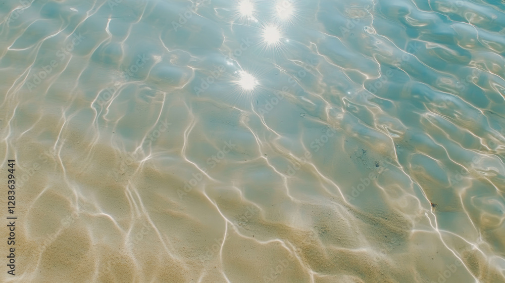 Fototapeta premium Sunlight reflections on clear water with golden ripples over a sandy beach, creating a shimmering pattern and a tranquil summer atmosphere
