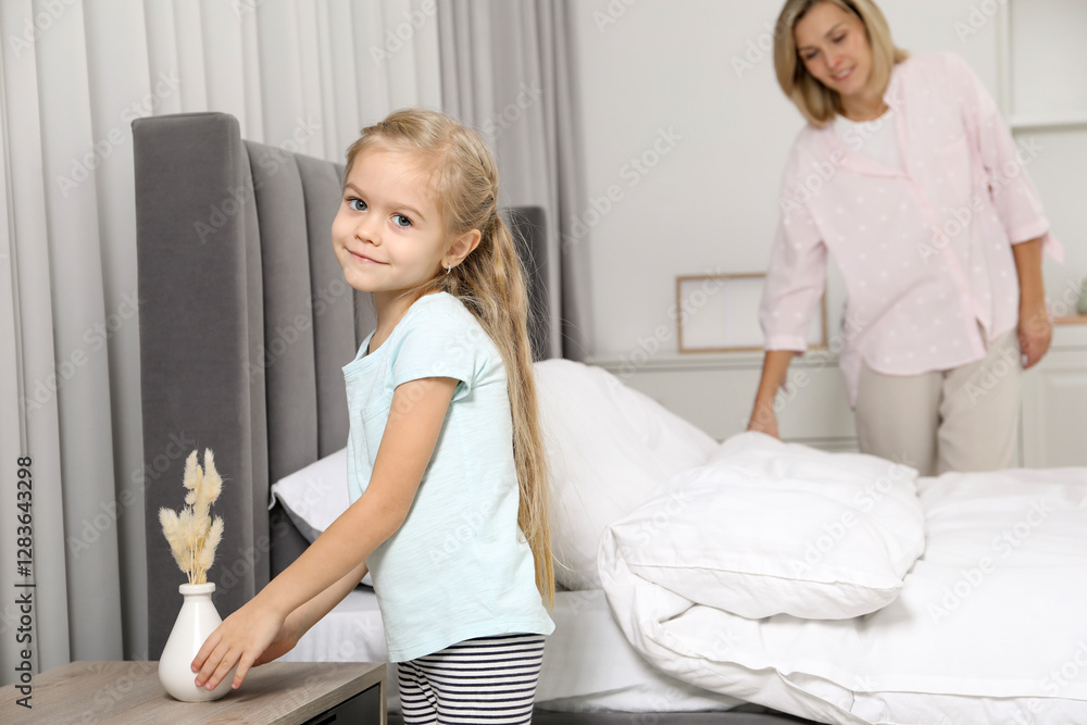Obraz premium Little girl helping her mother making bed at home
