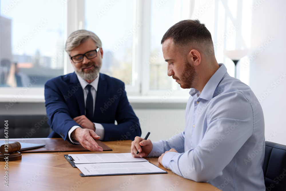 Client signing notarial paperwork during meeting with lawyer at wooden desk indoors, selective focus Client signing notarial paperwork during meeting with lawyer at wooden desk indoors, selective focus