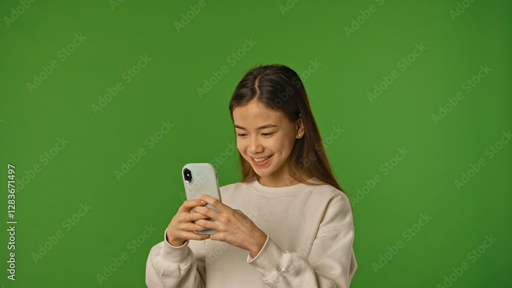 Asian girl child holding smartphone and typing, scrolling social media, positive expression, isolated on chroma key green screen studio background mockup. Asian girl child holding smartphone and typing, scrolling social media, positive expression, isolated on chroma key green screen studio background mockup.