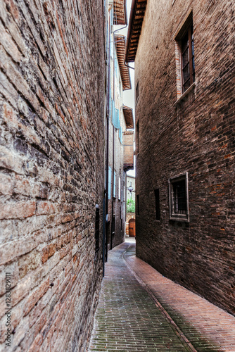 A narrow street in Urbino, a medieval town in Italy, where historic buildings with rustic stone facades tower on either side, creating a serene atmosphere.