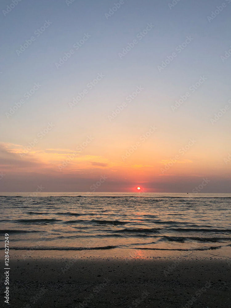 Sun sets over calm waters at a serene beach with soft waves and colorful sky in the evening Sun sets over calm waters at a serene beach with soft waves and colorful sky in the evening