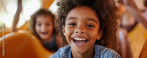 Joyful young girl laughing on playground slide with friend in background