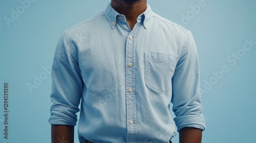 Close-up of a man's light blue, long-sleeved button-down shirt against a pale blue background.