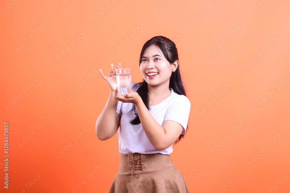 Happy young woman holding a glass of water, promoting hydration and healthy living. isolated on orange background Happy young woman holding a glass of water, promoting hydration and healthy living. isolated on orange background