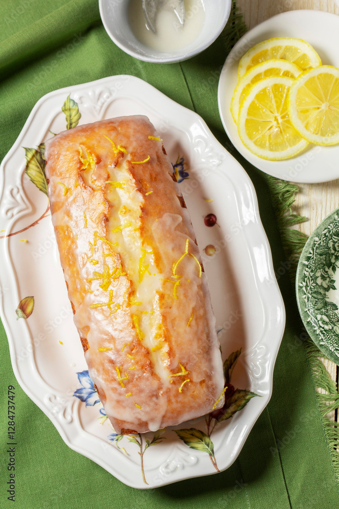 Aromatic lemon cake, covered with sugar icing and sprinkled with zest, served with tea.