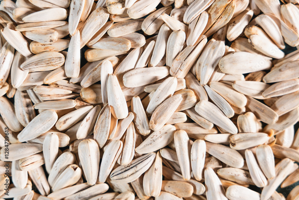 A detailed view of sunflower seeds with elongated beige shells and dark streaks, arranged densely to form a uniform and textured pattern. A detailed view of sunflower seeds with elongated beige shells and dark streaks, arranged densely to form a uniform and textured pattern.