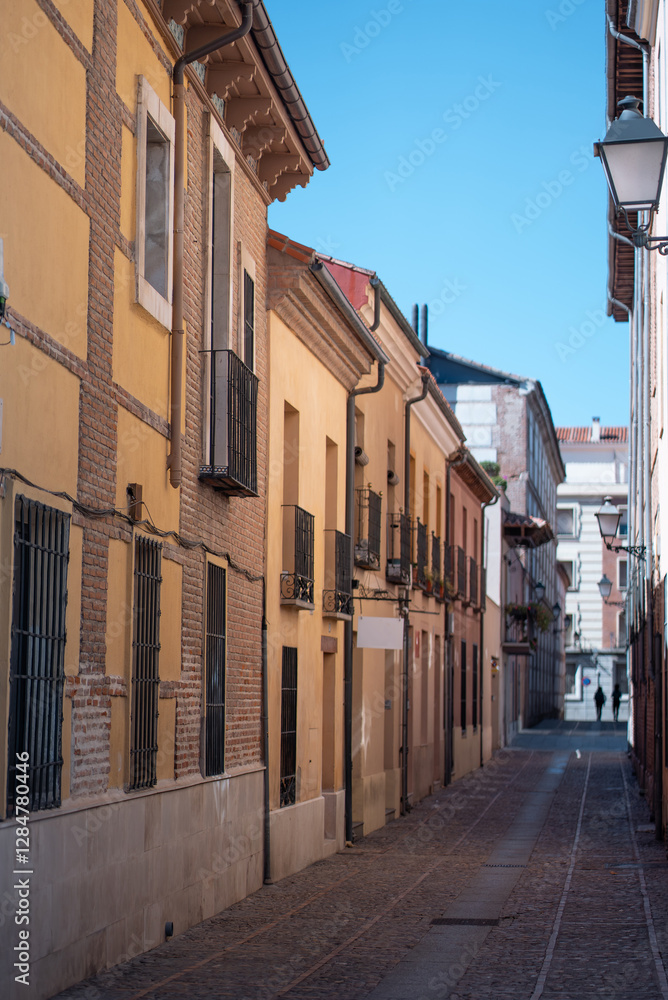 Fototapeta premium Narrow street lined with colorful buildings in a historic neighborhood on a sunny day, Alcala De Henares, Spain