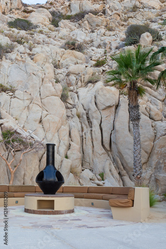 Black chimenea surrounded by a stone mountain and seating at the seaside resort with palm trees.