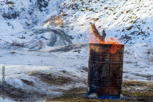 Flames rise from an old rusty barrel in a snowy winter landscape