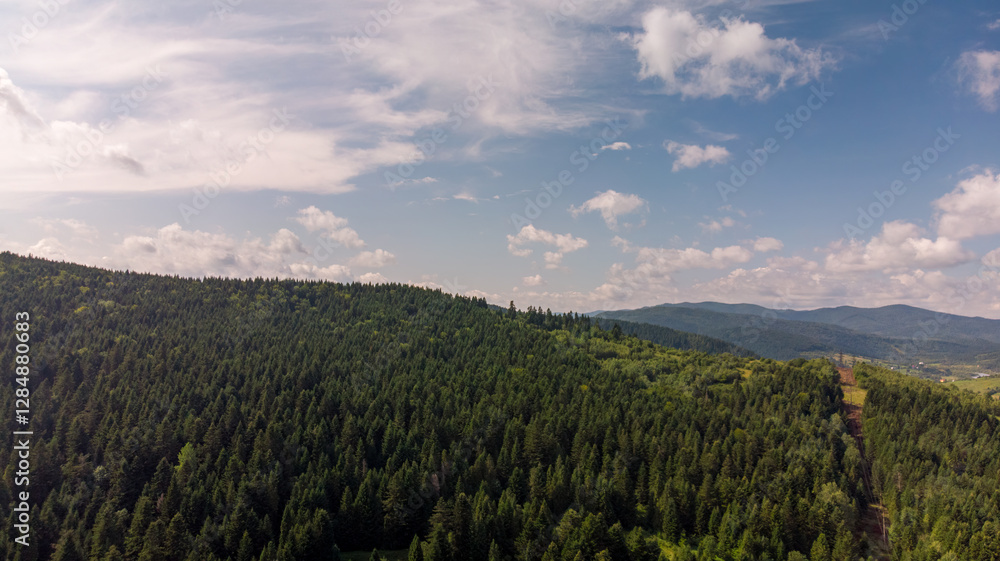 Naklejka premium Majestic Mountains, Lush Green Forests, And Soft White Clouds On A Sunny Day. Aerial View Showcasing The Stunning Beauty Of Nature From A High Perspective.