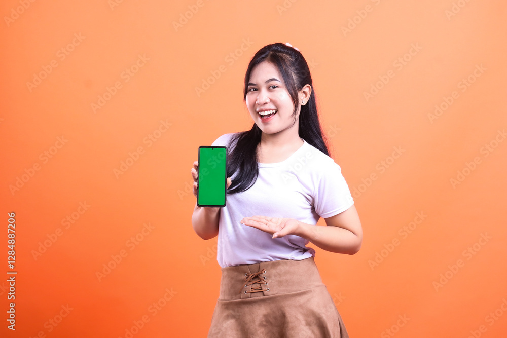 Smiling woman presents mobile phone with green screen against an orange background Smiling woman presents mobile phone with green screen against an orange background