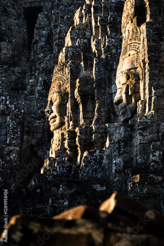 Wallpaper Mural At Peace.  Two faces on the Bayon Temple, Angkor, Cambodia are caught in early morning sunlight.  Dark stone surrounds the faces and blurred stones are in the foreground. Torontodigital.ca
