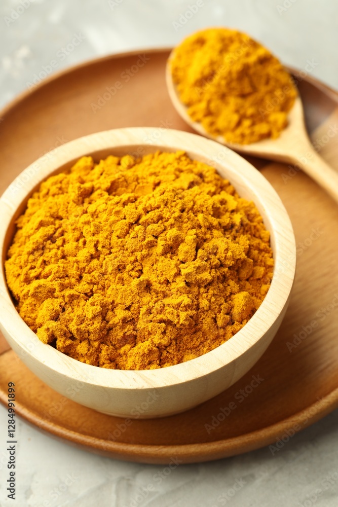 Turmeric powder in bowl and spoon on light grey table, closeup Turmeric powder in bowl and spoon on light grey table, closeup