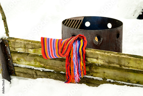 L’Assomption style sash or ceinture fléchée (traditional pattern) replica of the woven sashs worn by voyageurs during the fur trade shot on wooden bench with firepit in background photo