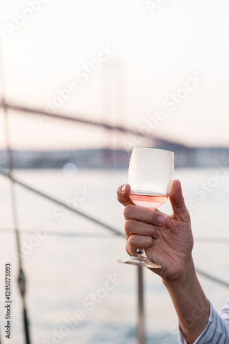 Hand holding a glass of rosé wine on a boat at sunset.