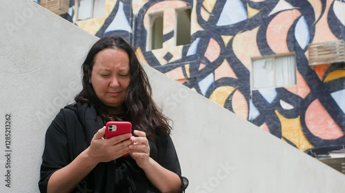 Wallpaper Mural Woman using smartphone while standing against building. Female is socializing online in city. She is wearing black dress during windy day. Torontodigital.ca