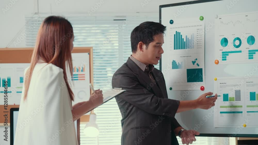 Business partners reviewing financial performance, analyzing charts on whiteboard during collaborative meeting in contemporary workspace Business partners reviewing financial performance, analyzing charts on whiteboard during collaborative meeting in contemporary workspace