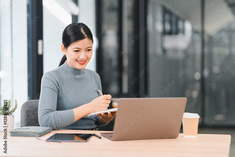 Woman working at desk with laptop, tablet, and coffee cup, smiling while writing notes. Woman working at desk with laptop, tablet, and coffee cup, smiling while writing notes.