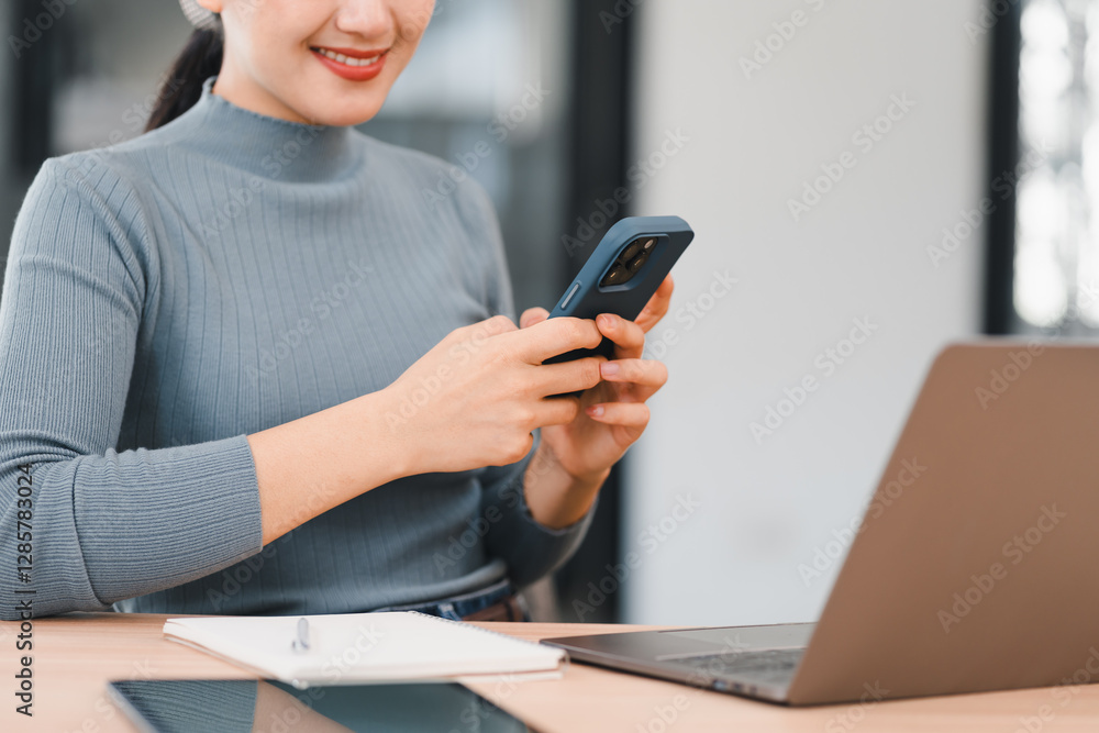 Woman smiling while using smartphone at desk with laptop, notebook, and tablet, creating productive atmosphere. Woman smiling while using smartphone at desk with laptop, notebook, and tablet, creating productive atmosphere.