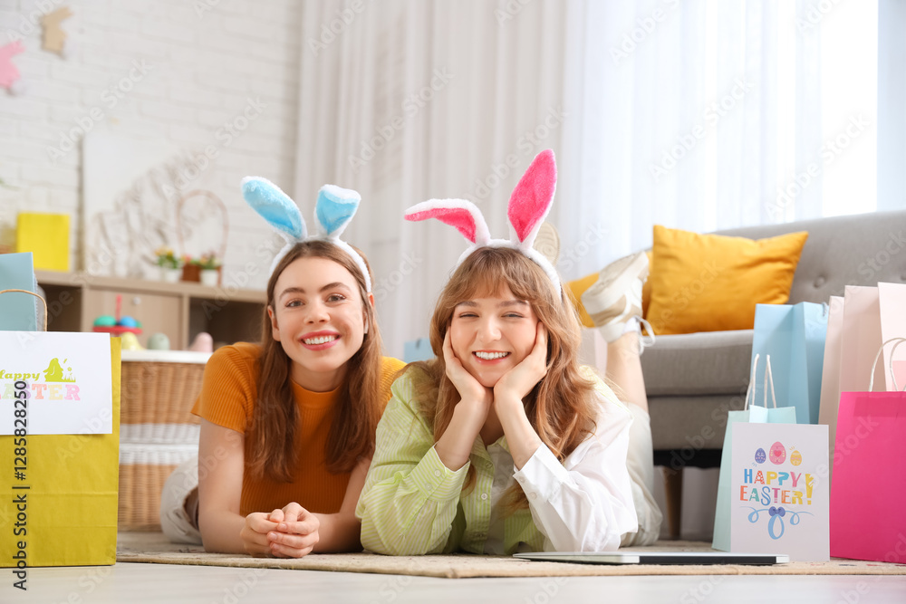 Φωτογραφία Happy young women in bunny ears headbands with laptop, paper bags and festive postcards for Easter lying on floor at home