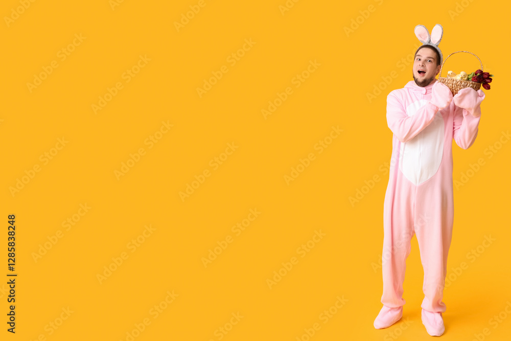 Obraz premium Surprised young man in bunny costume with Easter basket on yellow background