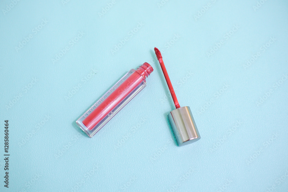 Naklejka premium Red lip gloss in elegant glass bottle with shiny lid, container with brush isolated on light blue background, red lipstick