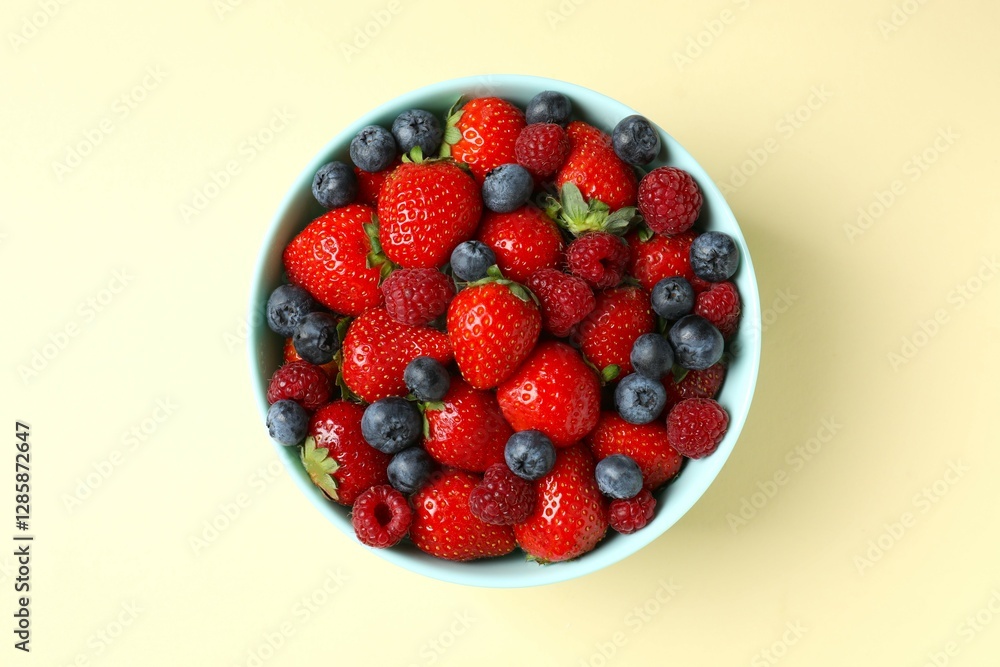 Different fresh ripe berries in bowl on color table, top view Different fresh ripe berries in bowl on color table, top view