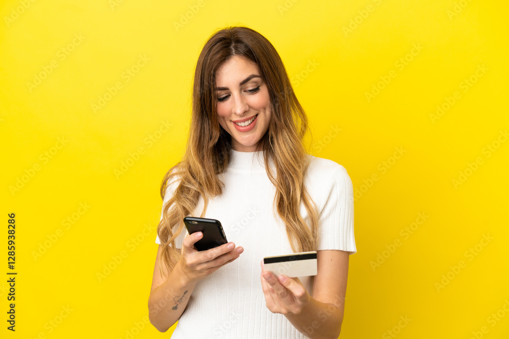 Caucasian woman isolated on yellow background buying with the mobile with a credit card Caucasian woman isolated on yellow background buying with the mobile with a credit card