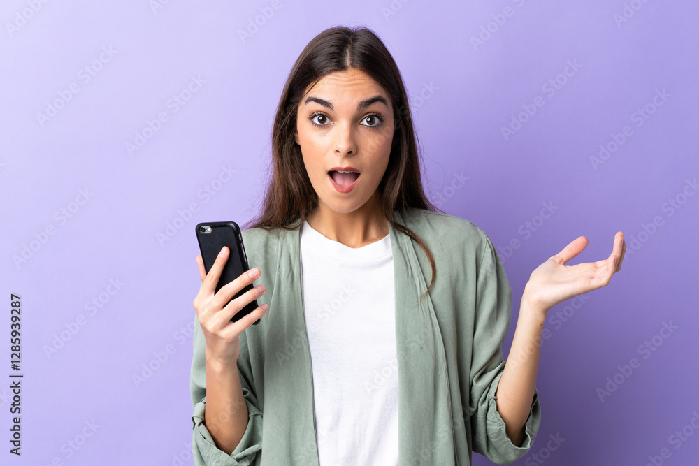 Young caucasian woman using mobile phone isolated on purple background with shocked facial expression Young caucasian woman using mobile phone isolated on purple background with shocked facial expression