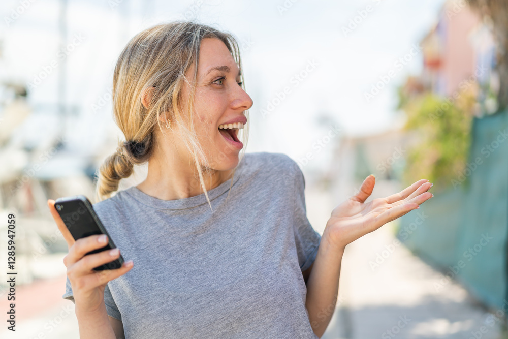 Young blonde woman using mobile phone at outdoors with surprise facial expression Young blonde woman using mobile phone at outdoors with surprise facial expression