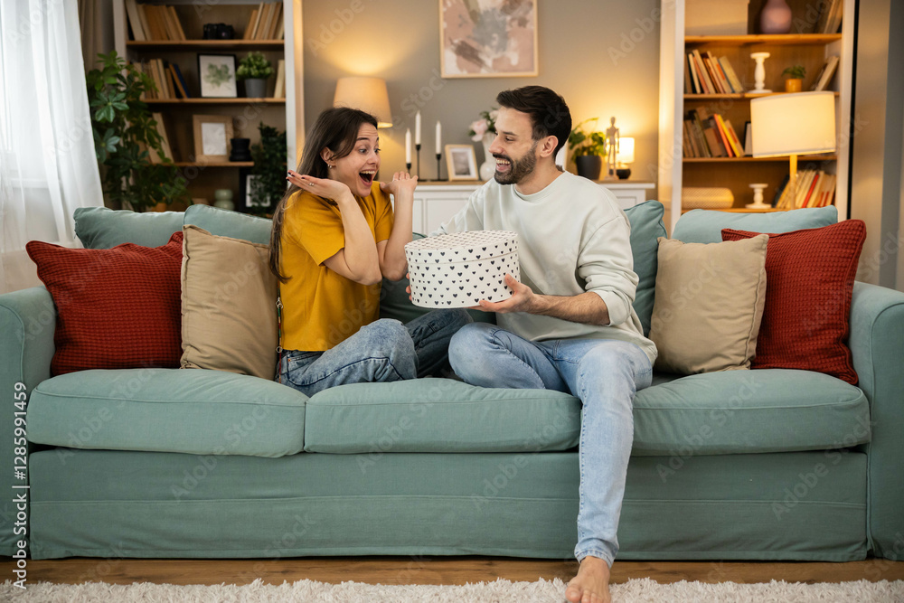 A woman's delighted expression captures the joy of receiving a heartfelt gift from her partner in a cozy living room setting. A woman's delighted expression captures the joy of receiving a heartfelt gift from her partner in a cozy living room setting.