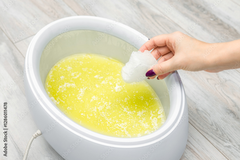 Manicurist melts paraffin in a paraffin bath. wax machine for paraffin therapy. spa manicure procedure. hand and foot spa. wax bath. body wax. hand holding a piece of paraffin. Manicurist melts paraffin in a paraffin bath. wax machine for paraffin therapy. spa manicure procedure. hand and foot spa. wax bath. body wax. hand holding a piece of paraffin.